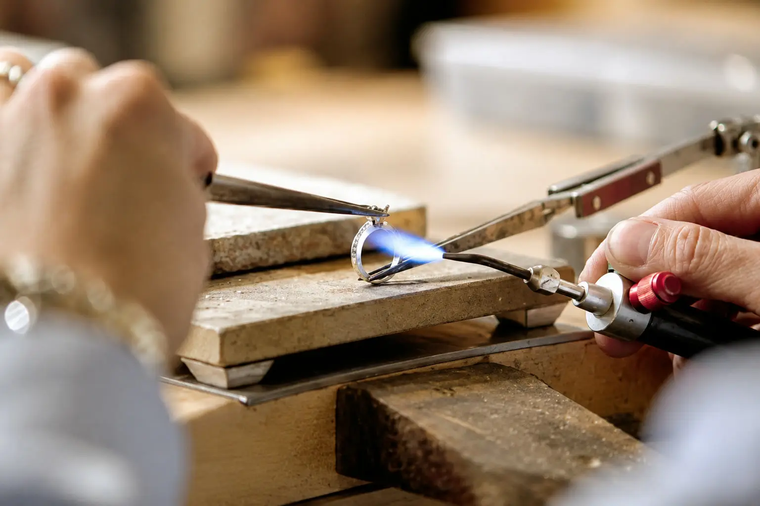 A diamond ring held in tweezers being resized with a jeweller’s torch at the workshop bench
